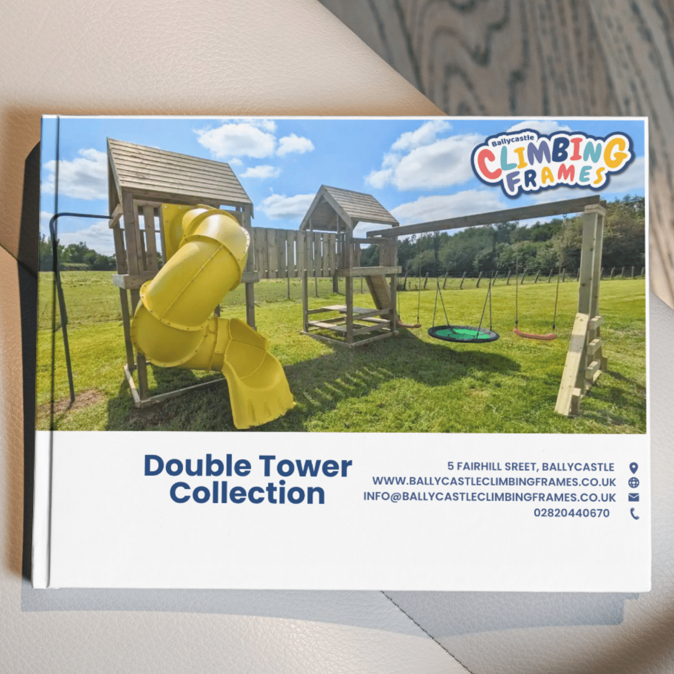 Double tower playground set with yellow slide and swings on grass, Ballycastle Climbing Frames logo and contact details.