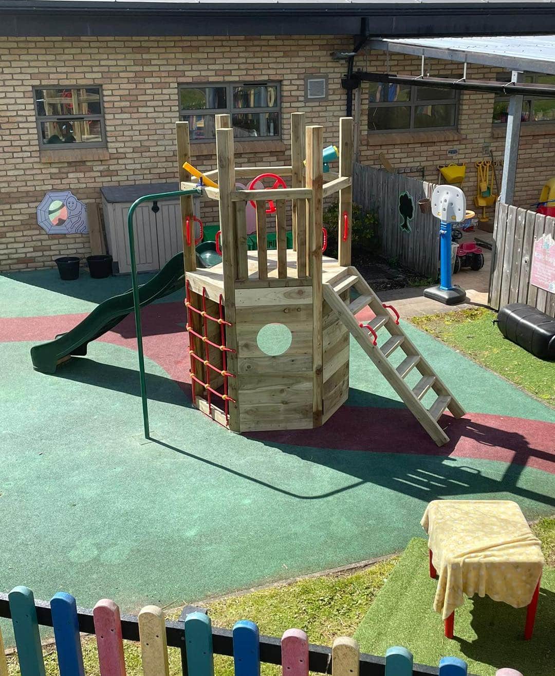 Wooden playground set with slide, ladder, and climbing net on a colorful outdoor play area.