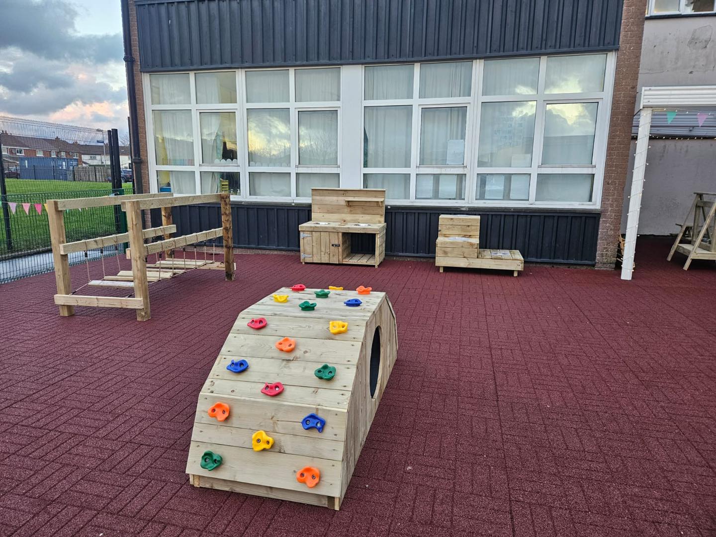 Outdoor playground area with climbing structure, benches, and red rubber flooring.