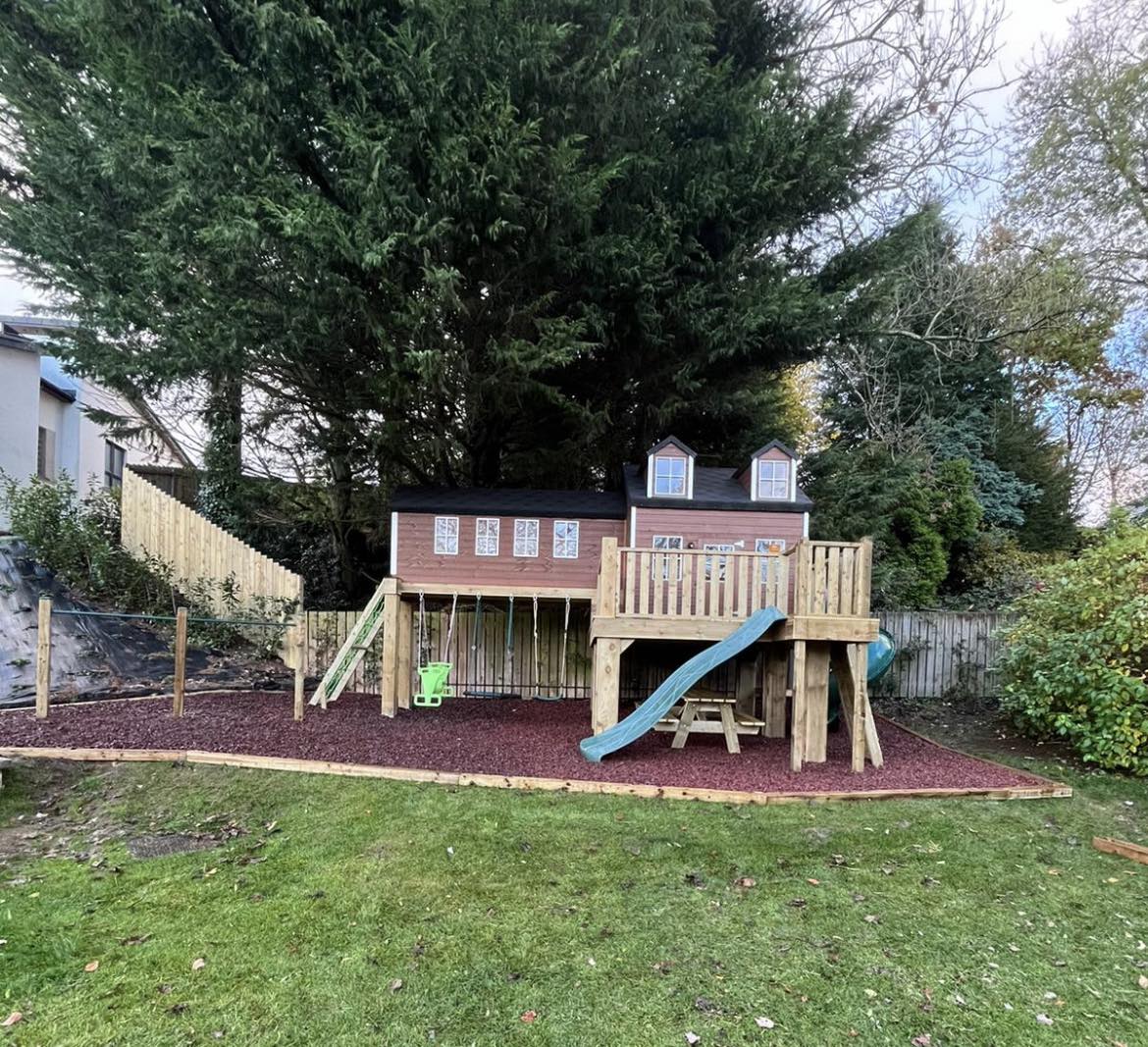 Two-storey playhouse with slide and swing set in a backyard.