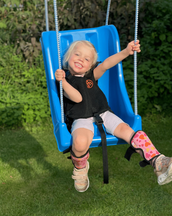 oung child enjoying an inclusive high-back swing with safety harness in an outdoor play setting.