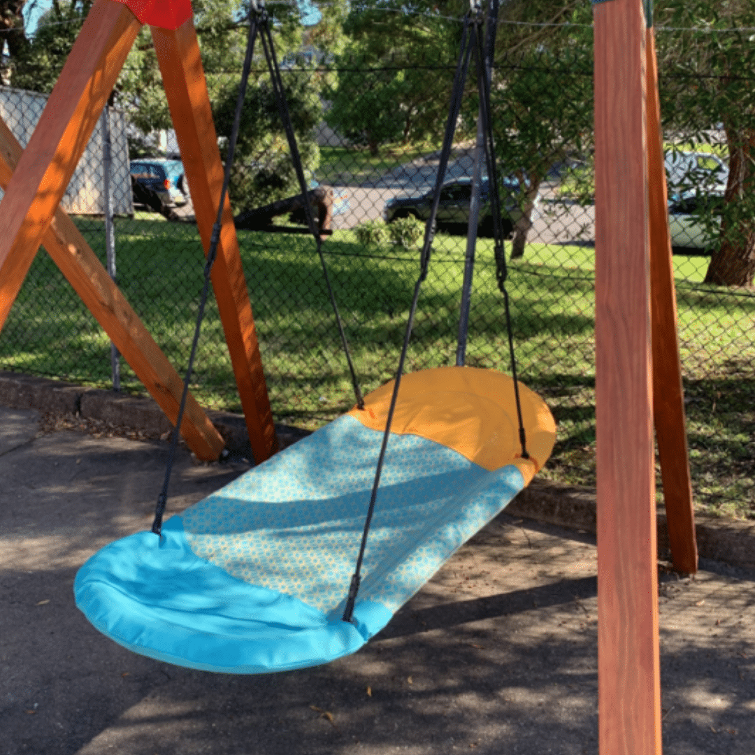 Colorful sensory boat swing with orange and blue fabric on a sturdy wooden frame, outdoors in a park.