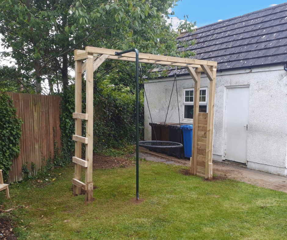 Wooden swing set with a climbing ladder in a backyard near a white building.