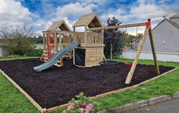 Children's playhouse with slides, swings, and climbing net in a backyard setting.