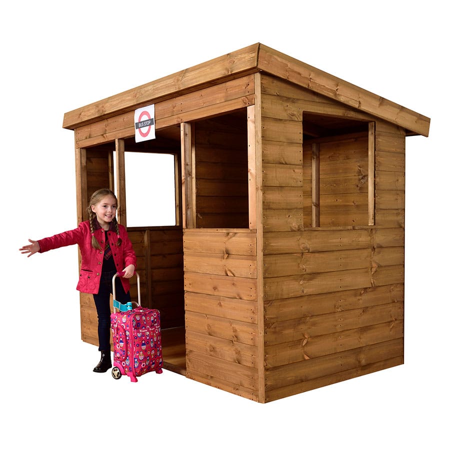 Child in red jacket playing by wooden playhouse bus stop with colorful suitcase.