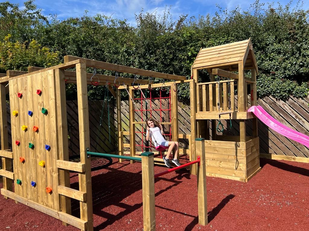 Child playing on a wooden playground set with climbing wall, slide, and swing.