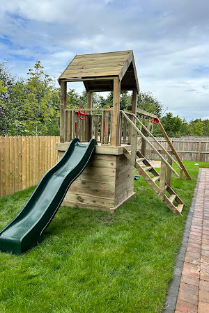Wooden playhouse with slide and ladder in a backyard.